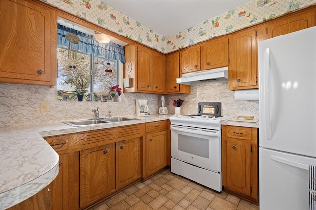 kitchen featuring light countertops, a sink, white appliances, under cabinet range hood, and wallpapered walls