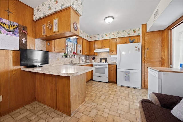 kitchen with under cabinet range hood, a peninsula, white appliances, light countertops, and brown cabinetry