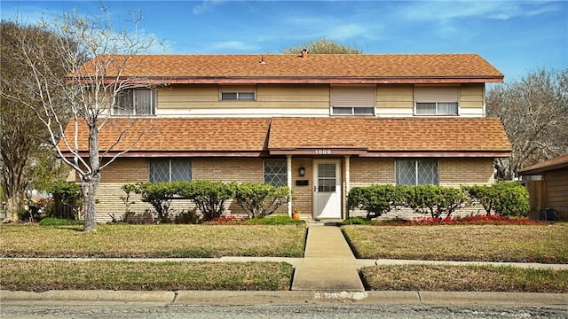 townhome / multi-family property with a shingled roof, a front yard, and brick siding