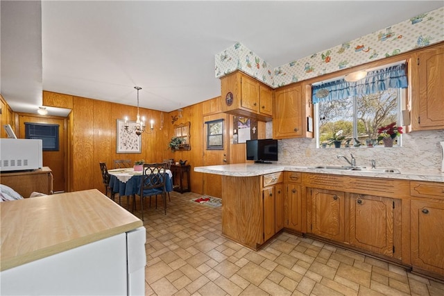 kitchen featuring white microwave, a peninsula, a sink, light countertops, and brown cabinets