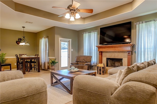 living room featuring a fireplace, ceiling fan, and a raised ceiling