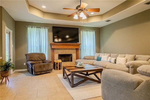 tiled living room with a fireplace, ceiling fan, and a raised ceiling