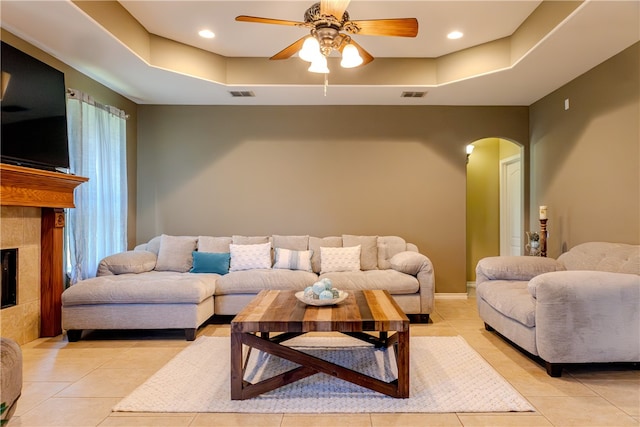 tiled living room with a tile fireplace, ceiling fan, and a raised ceiling