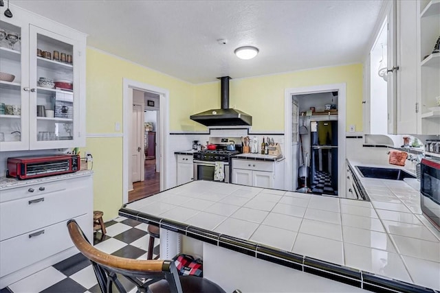 kitchen with tile countertops, wall chimney range hood, sink, stainless steel gas range, and white cabinetry