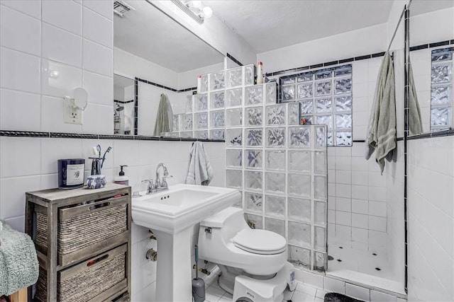 bathroom featuring a textured ceiling, sink, tiled shower, tile walls, and toilet