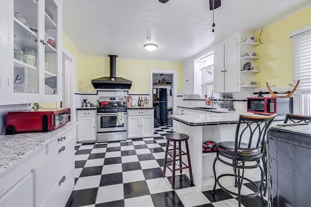 kitchen with white cabinetry, a kitchen breakfast bar, black fridge, ventilation hood, and stainless steel stove