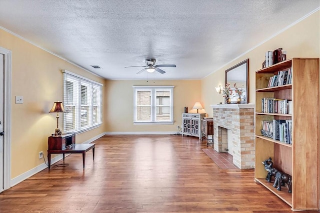 living room featuring ceiling fan, a fireplace, wood-type flooring, and a textured ceiling