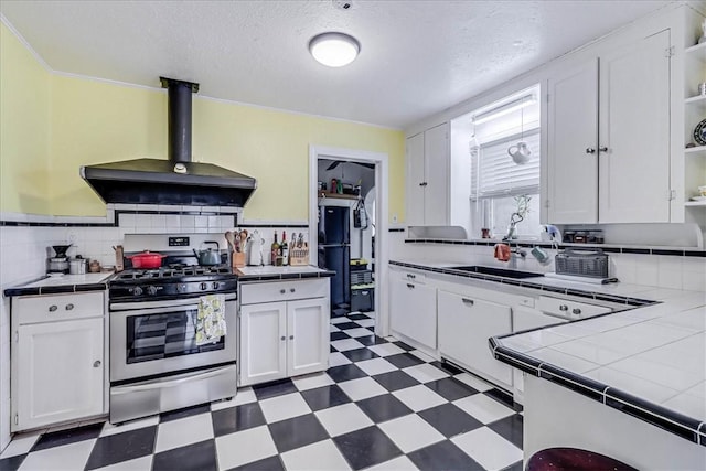 kitchen with stainless steel gas stove, white cabinetry, tile counters, and exhaust hood