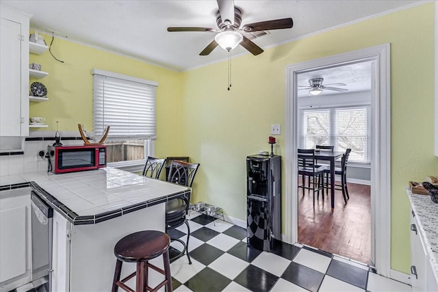 kitchen with tile countertops, kitchen peninsula, ceiling fan, a kitchen bar, and white cabinetry