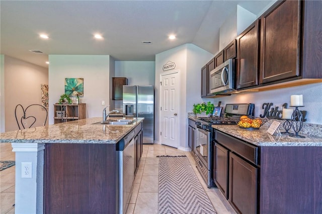 3922 Jayden Dr, Corpus Christi, TX 78410 - kitchen featuring stainless steel appliances, a center island with sink, dark brown cabinetry, light stone counters, and light tile patterned floors