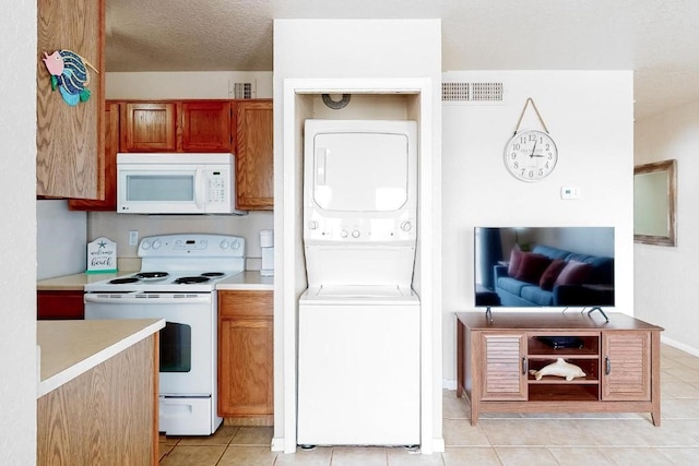 kitchen featuring a textured ceiling, white appliances, stacked washer and dryer, and light tile patterned floors