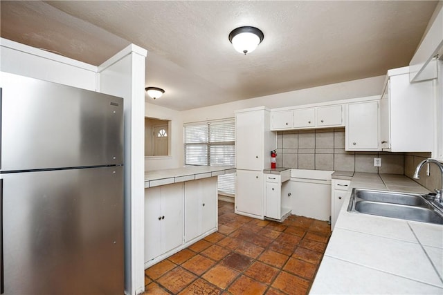 kitchen with tile countertops, a sink, white cabinets, freestanding refrigerator, and tasteful backsplash