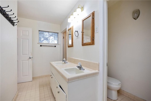 bathroom with toilet, double vanity, a sink, and tile patterned floors