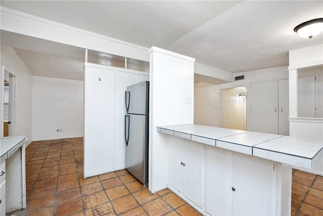 kitchen with a peninsula, visible vents, white cabinets, freestanding refrigerator, and tile counters