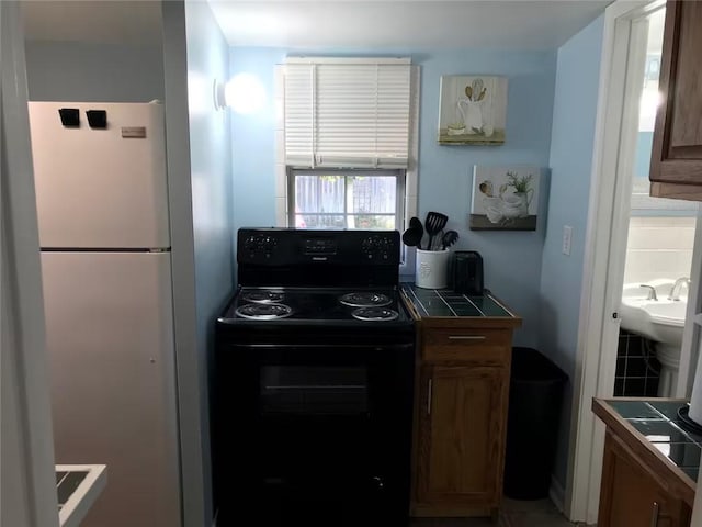 kitchen with freestanding refrigerator, tile countertops, black range with electric stovetop, and brown cabinetry