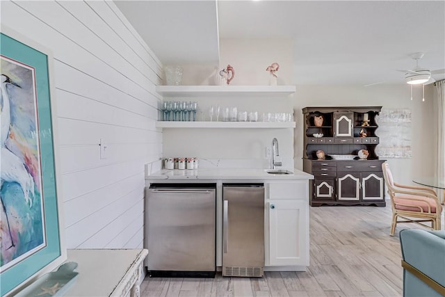 bar with refrigerator, light hardwood / wood-style floors, stainless steel refrigerator, sink, and white cabinetry