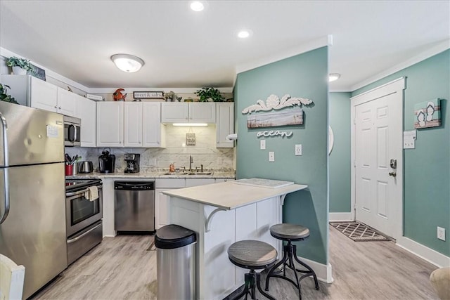 kitchen featuring a breakfast bar, sink, white cabinets, stainless steel appliances, and backsplash