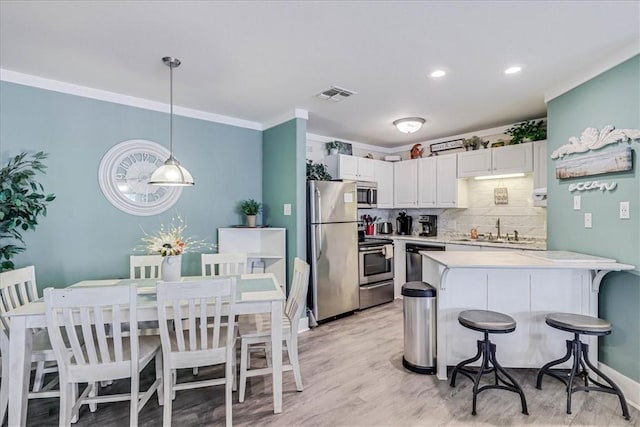 kitchen featuring sink, a breakfast bar area, appliances with stainless steel finishes, white cabinetry, and decorative light fixtures