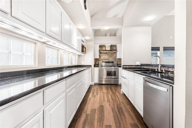 kitchen featuring wall chimney range hood, sink, dark wood-type flooring, appliances with stainless steel finishes, and white cabinetry