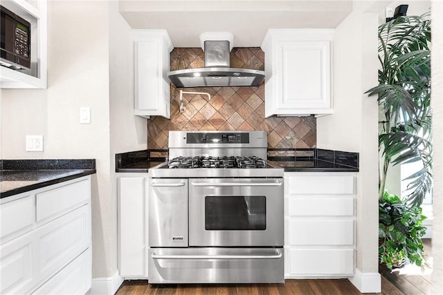 kitchen featuring white cabinets, dark hardwood / wood-style flooring, dark stone counters, range with two ovens, and wall chimney range hood