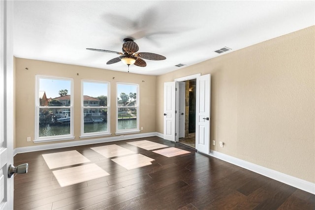 empty room featuring dark wood-type flooring, ceiling fan, and a water view