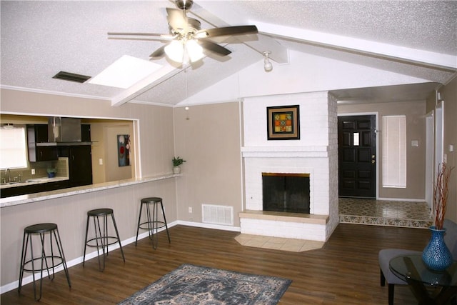 living room with vaulted ceiling with beams, ceiling fan, a textured ceiling, and a brick fireplace