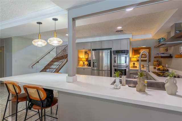 kitchen featuring kitchen peninsula, appliances with stainless steel finishes, a kitchen breakfast bar, a textured ceiling, and hanging light fixtures