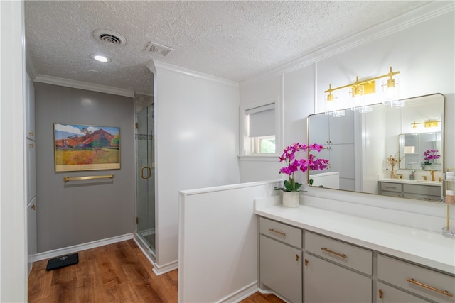 bathroom with wood-type flooring, a textured ceiling, ornamental molding, vanity, and walk in shower