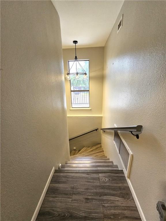 stairway with visible vents, a textured wall, baseboards, and wood finished floors