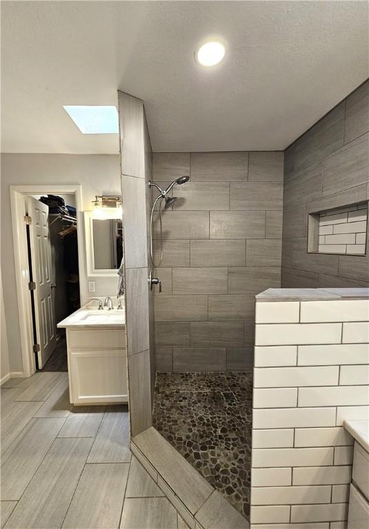 full bath featuring a skylight, wood finish floors, walk in shower, and vanity