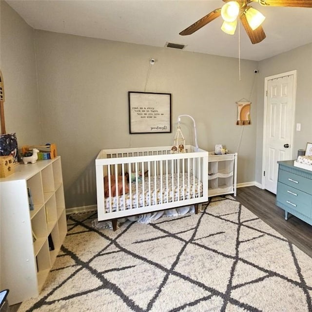 bedroom featuring wood finished floors, a ceiling fan, visible vents, baseboards, and a nursery area