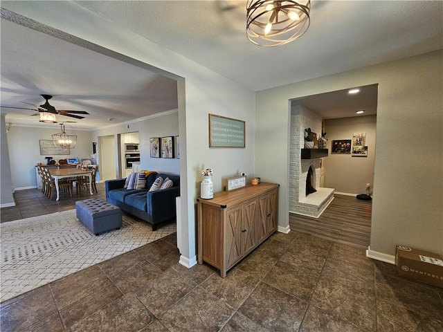 living room with ceiling fan with notable chandelier, a fireplace, and baseboards