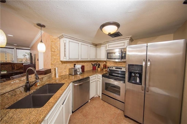 kitchen featuring visible vents, a sink, light stone counters, appliances with stainless steel finishes, and hanging light fixtures