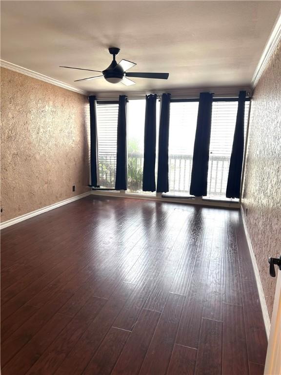 empty room featuring dark wood finished floors, a ceiling fan, a textured wall, and ornamental molding