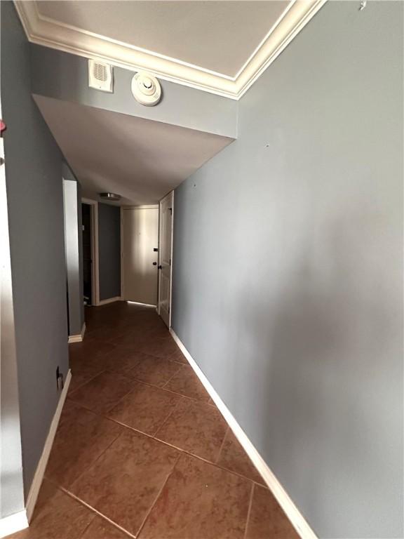 corridor with baseboards, dark tile patterned flooring, and crown molding