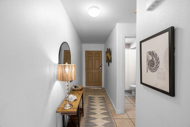 hallway with light tile patterned floors, visible vents, and baseboards