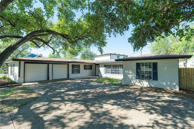 single story home featuring fence, aphalt driveway, brick siding, and a garage