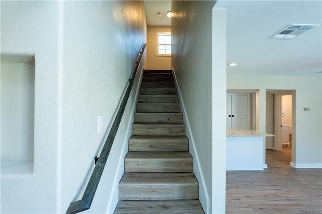 staircase featuring baseboards, visible vents, wood finished floors, and recessed lighting