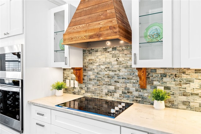 kitchen featuring white cabinetry, light stone counters, premium range hood, backsplash, and black electric stovetop