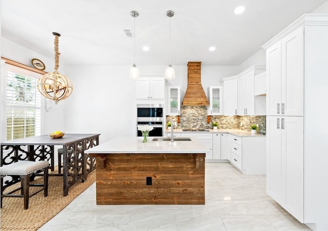 kitchen featuring pendant lighting, premium range hood, an island with sink, and appliances with stainless steel finishes