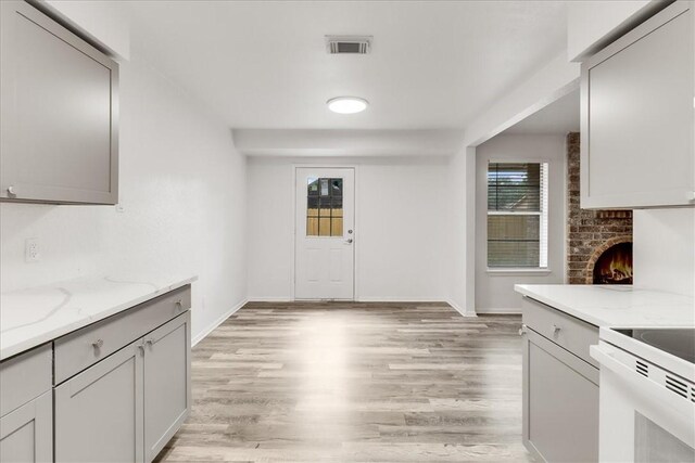 2108 Matagorda Dr, Portland, TX 78374 - kitchen featuring light wood-style floors, light stone countertops, a brick fireplace, and gray cabinetry