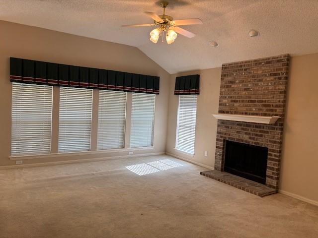 unfurnished living room featuring carpet flooring, a brick fireplace, a textured ceiling, vaulted ceiling, and ceiling fan