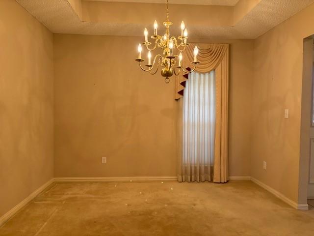 empty room with a textured ceiling, carpet floors, an inviting chandelier, and a healthy amount of sunlight