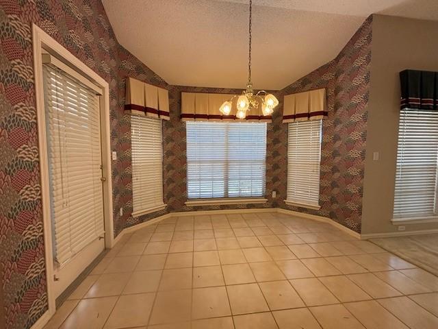 unfurnished dining area featuring a textured ceiling, light tile patterned floors, lofted ceiling, and a notable chandelier