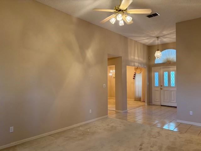 carpeted empty room with a high ceiling and ceiling fan with notable chandelier