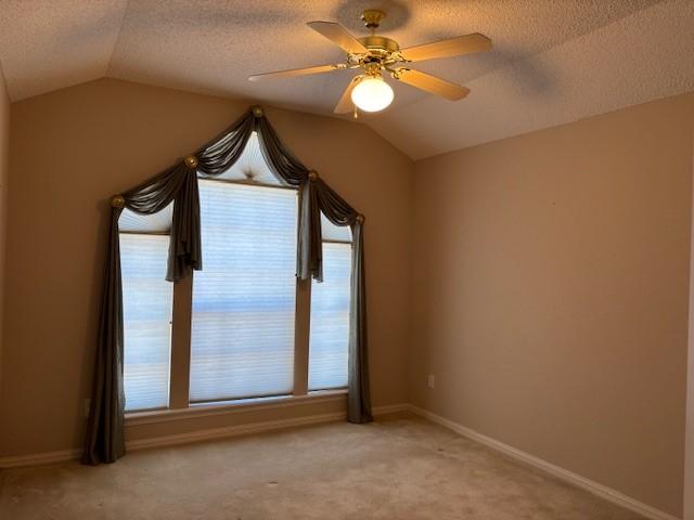 carpeted spare room with a textured ceiling, ceiling fan, and vaulted ceiling