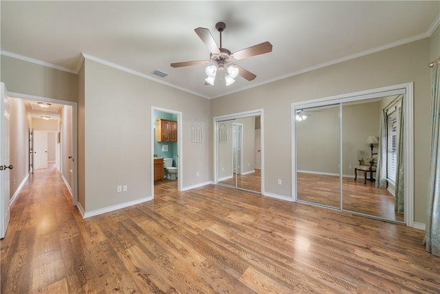 unfurnished bedroom with baseboards, visible vents, wood finished floors, crown molding, and two closets