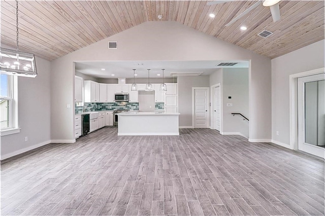 kitchen featuring white cabinets, pendant lighting, light wood-type flooring, a kitchen island, and appliances with stainless steel finishes