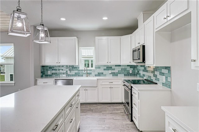 kitchen featuring appliances with stainless steel finishes, light wood-type flooring, sink, decorative light fixtures, and white cabinets