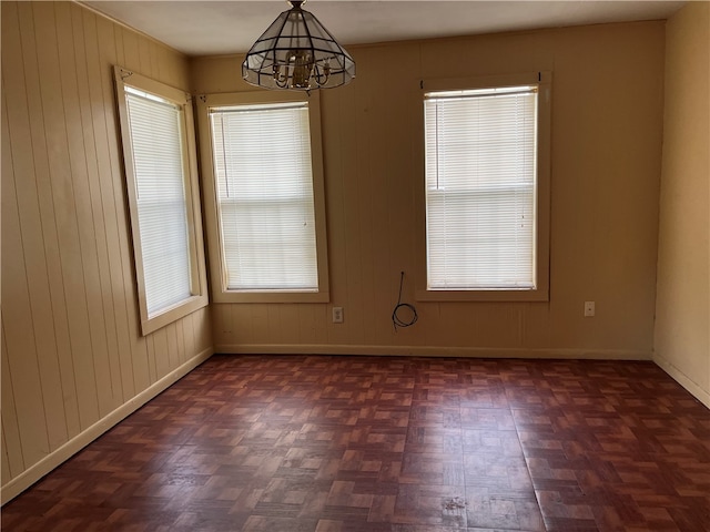 unfurnished room featuring wooden walls, a healthy amount of sunlight, dark parquet floors, and an inviting chandelier